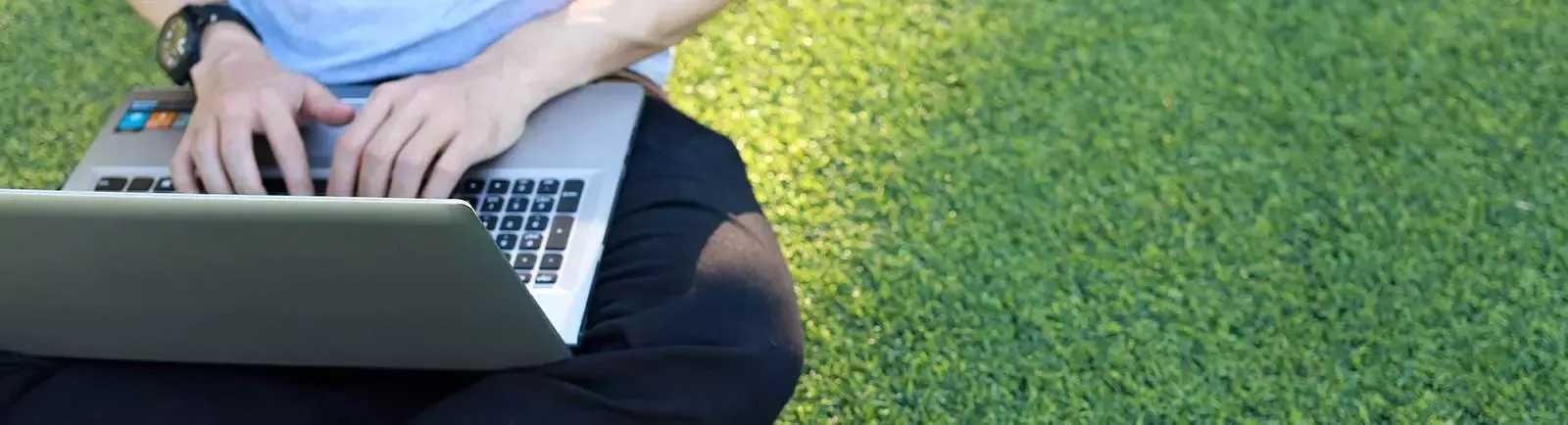 person sitting on grass typing on a laptop